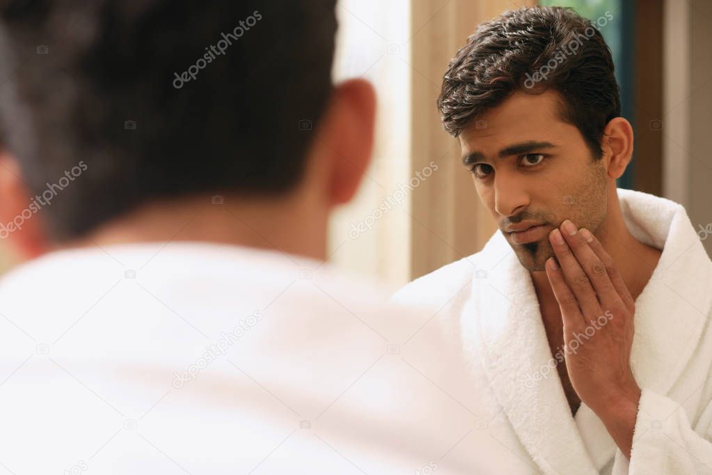 Man in bathrobe looking at himself in mirror