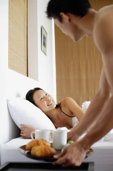 Женщина в постели, мужчина устанавливает поднос для завтрака — стоковое фото