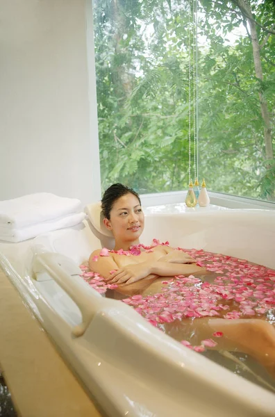 Kvinna i badkar, blommor flytande — Stockfoto