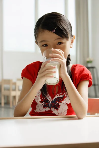 Ragazza seduta a tavola, bere un bicchiere di latte — Foto Stock