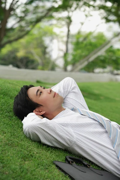 Affärsman liggande på gräset i parken — Stockfoto