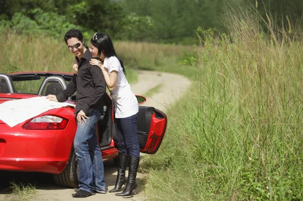 Пара стоящих рядом с красным спортивным автомобилем — стоковое фото