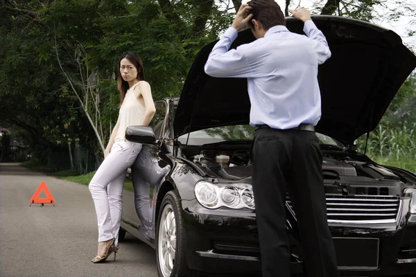 Man looking under car hood of broken down car