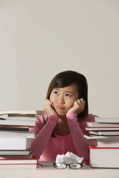 Jonge vrouw zit aan bureau met boeken op zoek triest. — Stockfoto