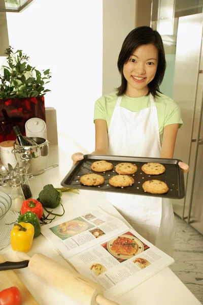 Young woman holding out baking tray — Stock Photo, Image