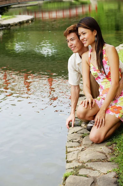 Couple crouching next to pond