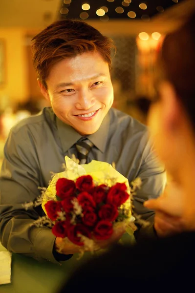 Pareja hombre sosteniendo hacia fuera ramo floral — Foto de Stock