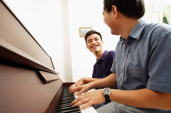 Pojke spela på piano med far — Stockfoto