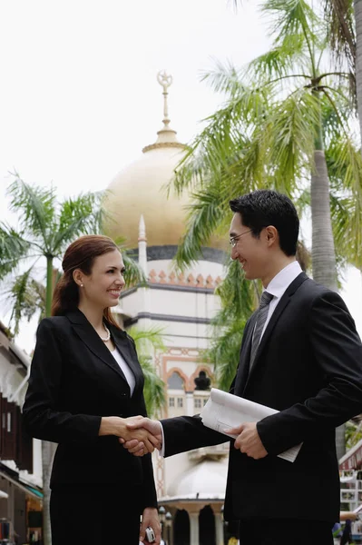 Empresario y empresaria estrechando la mano, Mezquita en el fondo — Foto de Stock