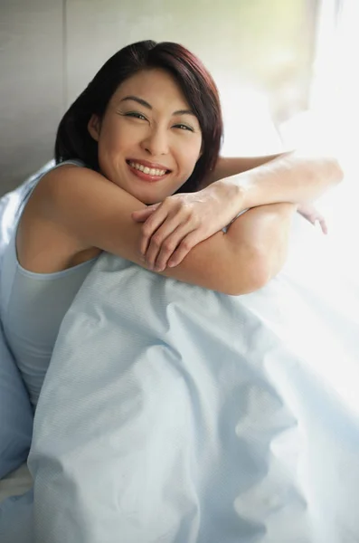 Женщина на кровати обнимает колени — стоковое фото