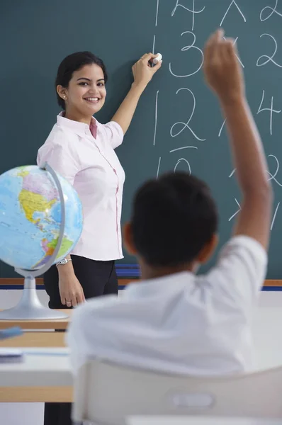 Teacher at chalkboard boy raises hand — Stock Photo, Image