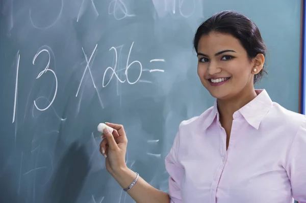 Вчителька посміхається, як вона пише на дошці — стокове фото