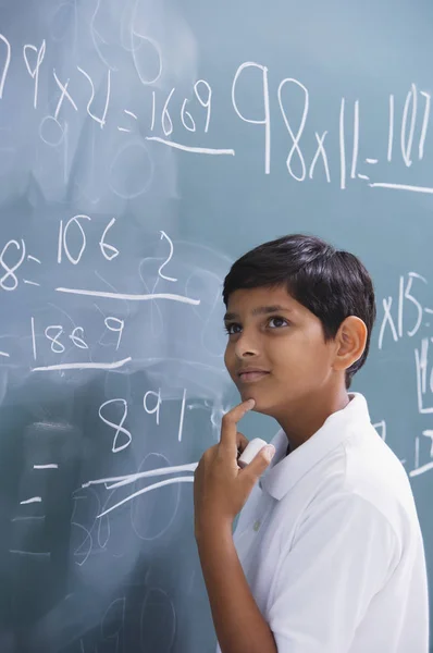 Boy at chalkboard, finger on chin — Stock Photo, Image