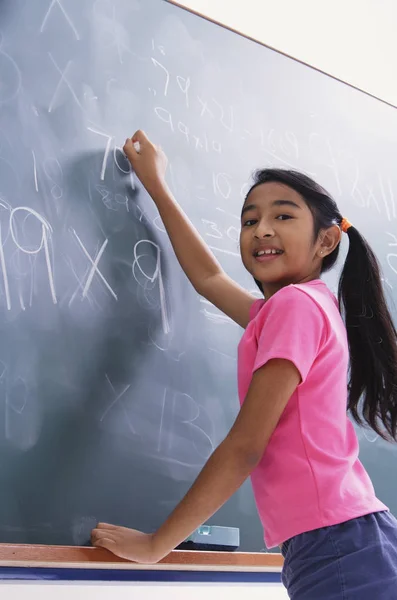 Girl working at chalkboard, facing camera — Stock Photo, Image