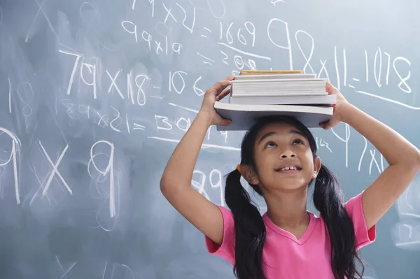 Ragazza con libri accatastati sulla testa, guardando in alto — Foto Stock