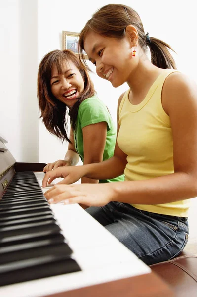 Girl playing on piano with mother Stock Image