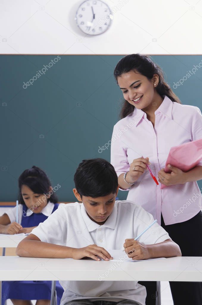 two students at desk, teacher standing