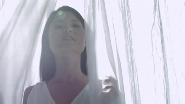 Женщина стоит между белыми занавесками — стоковое видео
