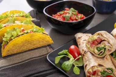 Çeşitli karışık Meksika yemekleri. Taco, burrito, fajita, karanlık bir masada salsa.