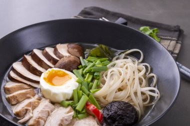 Japon eriştesi çorbası, tavuk, mantar, makarna, yumurta ve siyah arkaplanda soğan.