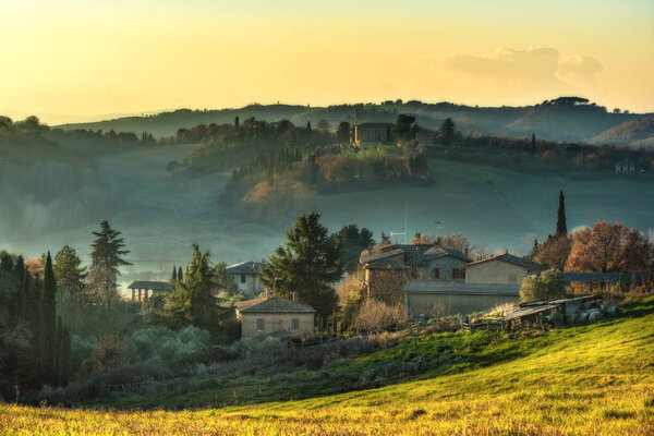 Fields and buildings in the mist at sunset.