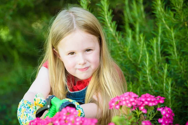 Hermosa chica rubia regando flores, césped en una hermosa soleada — Foto de Stock