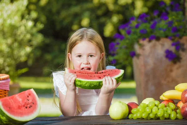 Šťastná dívka s velkým červeným dílek melounu sedí na rustikální ta — Stock fotografie