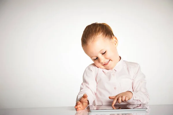 Menina bonito pouco e sorridente brinca com um tablet — Fotografia de Stock