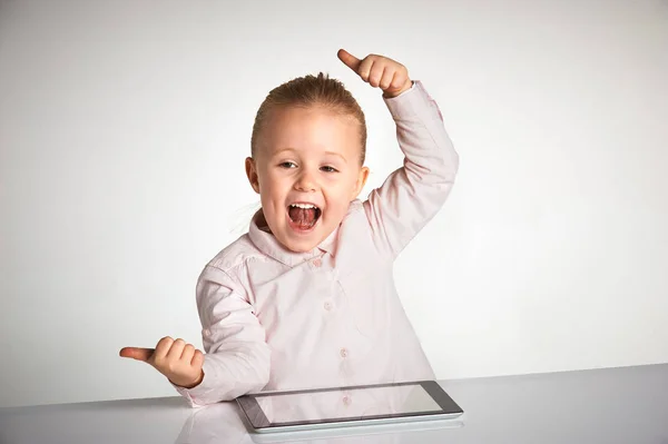 Menina bonito pouco e sorridente brinca com um tablet — Fotografia de Stock