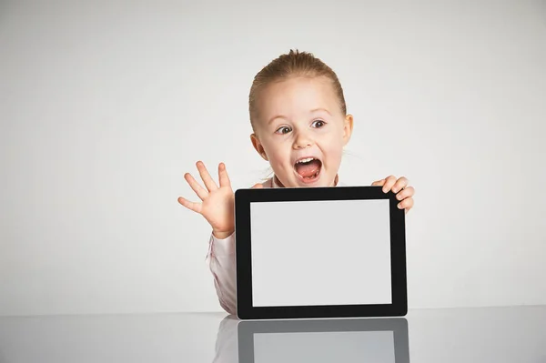 Menina bonito pouco e sorridente brinca com um tablet — Fotografia de Stock