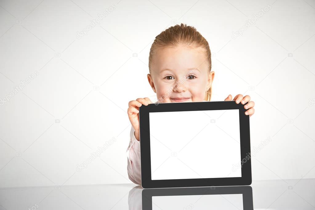 Cute little and smiling girl plays with a tablet