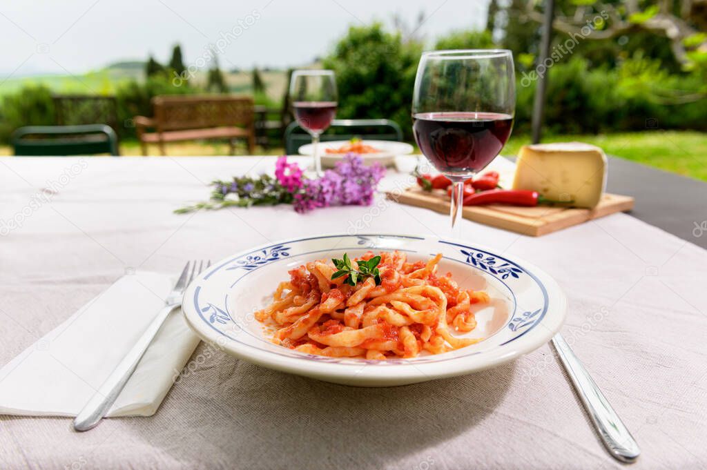 Italian dish, handmade spaghetti pasta, pici with tomato sauce on a table in the garden outdoors.