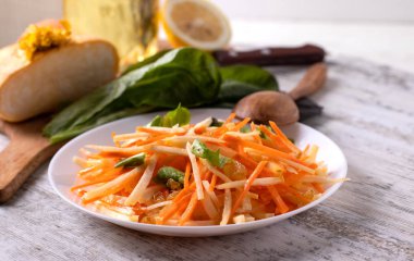 Şalgam, havuç, yeşil marul ve kuru üzümlü bir tabak salata. Tahta bir arka planda izole edilmiş beyaz bir tabakta sebze salatası..