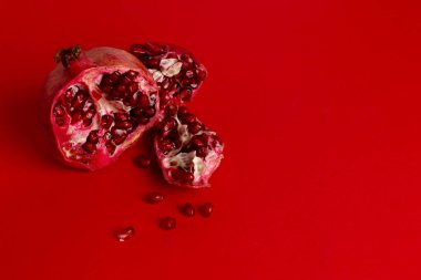 Kırmızı arkaplanda kırmızı nar izole edilmiş. Kırmızı arka planda nar tohumları. Nar parçaları etrafa saçılmış. Yatay oryantasyon. Metin için alanı kopyala.