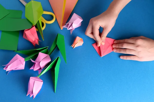 Anneler günü hediyesi. Bir çocuğun elleri. Anneler Günü, mutlu yıllar, 8 Mart, Kadınlar Günü, Sevgililer Günü. Mavi arka planda origami renkli kağıttan yapılmış bir buket lale. Boşluğu kopyala.