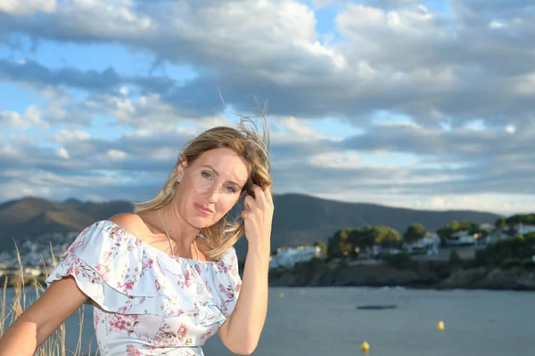 Mujer sentada frente a un paisaje costero del norte del Mediterráneo en una tarde de verano con viento mirando a la cámara con espacio para copiar — Foto de Stock