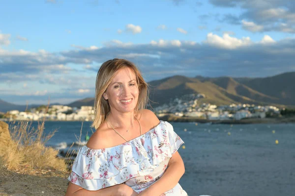 Happy woman sitting in front of a coastal landscape of the northern mediterranean on a summer afternoon with wind looking at the camera smiling with copy space — Stock fotografie