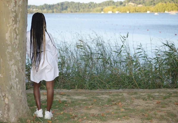검정 머리에 긴 검은색 과 금발 머리를 한 소녀가 나무 위에 앉아 뒤에 있는 호수를 바라봅니다. — 스톡 사진