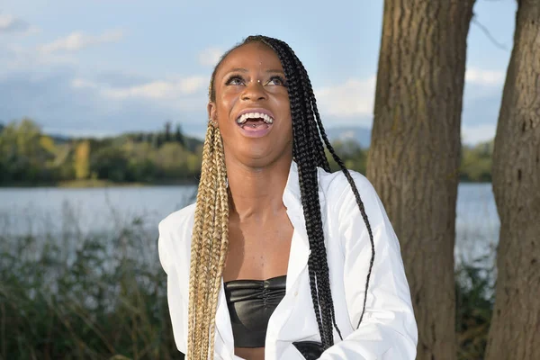 Gelukkig zwart afro meisje poses lachen met lange zwart en blond vlechten met een meer in de achtergrond — Stockfoto