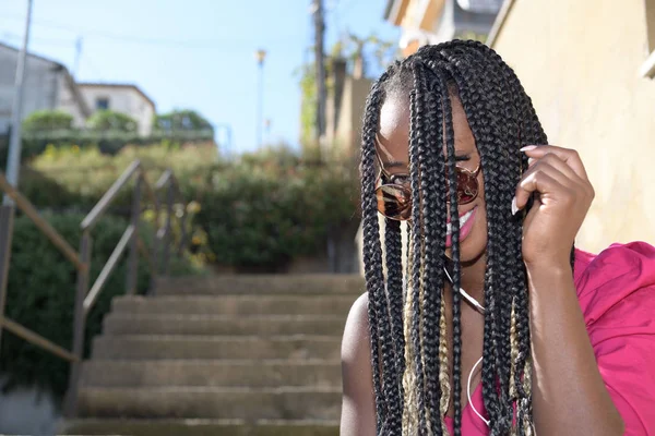 Retrato de una chica negra afro-estilo feliz con largas trenzas negras y rubias y gafas de sol sonriendo y mirando a la cámara —  Fotos de Stock