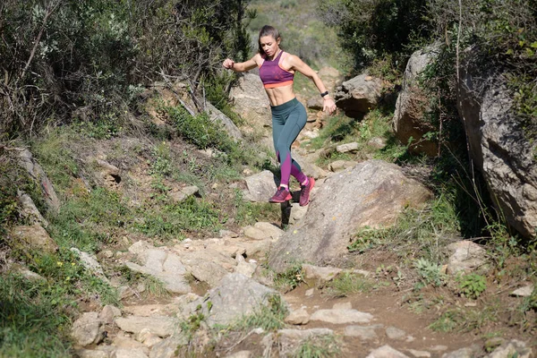 Sportswoman runs down a rock-filled mountain trail while doing her daily workout ロイヤリティフリーのストック写真