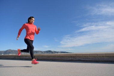 Sporcu kadın deniz kenarındaki güvertede koşuyor.