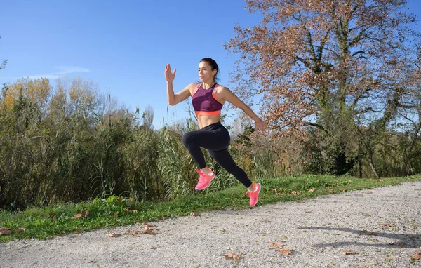 Sportswoman jumps while running along a trail in a natural environment