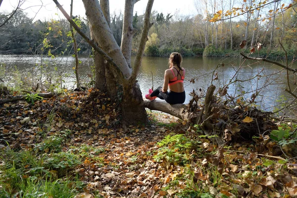 Sportswoman rests and sits by the river after her daily training