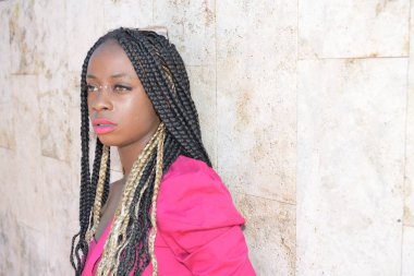 Uzun siyah ve sarı örgülü, güneş gözlüğü takan Afro-stil siyah kız bir duvarda dinleniyor ve hayaller kuruyor.