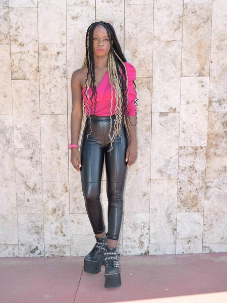 Afro-stil svart flicka med långa svarta och blondiner flätor bär stora skor, läder byxor och solglasögon vilar på en vägg och tittar på kameran — Stockfoto