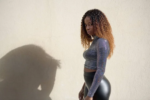 A happy black afro girl with curly brown hair standing looking at the camera with a serious expression. Her shadow is onto the wall ロイヤリティフリーのストック画像