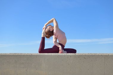 Açık havada yoga yapan sağlıklı bir kadının portresi. Güneşli bir günde arka planda mavi gökyüzü olan bir kadın asana çalışıyor.