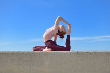 Açık havada yoga yapan sağlıklı bir kadının portresi. Güneşli bir günde arka planda mavi gökyüzü olan bir kadın asana çalışıyor.