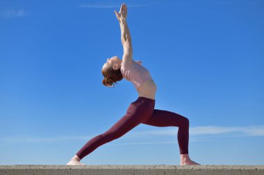 Açık havada yoga yapan sağlıklı bir kadının portresi. Güneşli bir günde arka planda mavi gökyüzü olan bir kadın asana çalışıyor.